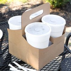 four white cups in a brown paper bag on a black metal table with utensils