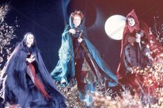 three women dressed in medieval costumes walking through the woods at night with full moon behind them