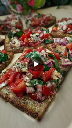 several slices of pizza with tomatoes, onions and spinach on them sitting on a cutting board