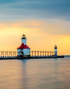 a light house sitting on the end of a pier next to the ocean at sunset