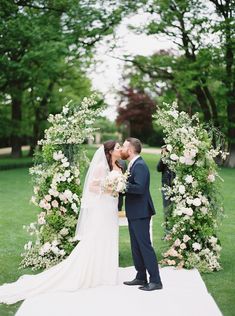 a bride and groom kissing in front of an arch with flowers