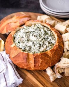 a bread bowl filled with spinach dip surrounded by crackers on a cutting board