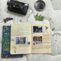 an open book sitting on top of a bed next to a camera and other items