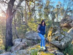 a woman standing on top of a rock covered hillside next to trees and rocks with moss growing on them