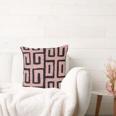 a pink and black pillow sitting on top of a white couch next to a vase with flowers