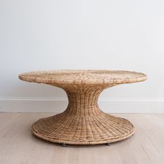 a round wicker table with wheels on the bottom, against a plain white wall