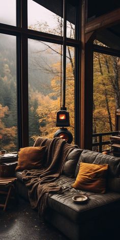 a living room filled with furniture and large windows overlooking the trees in the fall season