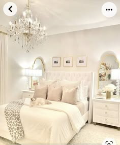 a white bedroom with a chandelier hanging from the ceiling and pillows on the bed