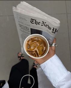 a person holding up a cup of coffee with the news paper in front of them