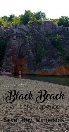 a woman standing on top of a sandy beach next to a cliff covered in trees