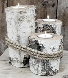 three white birch logs with rope wrapped around them and lit candles in front of a wooden wall