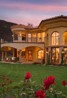 a large home in the middle of a lush green field with palm trees and mountains behind it