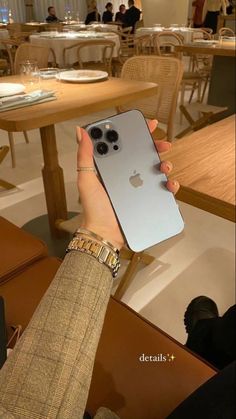 a person holding up an iphone in front of a table with chairs and plates on it