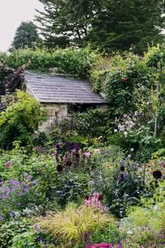 an old building surrounded by flowers and plants in the middle of a garden with lots of greenery