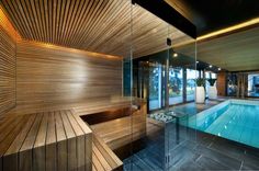 an indoor swimming pool surrounded by glass walls and wooden steps leading to the upper level