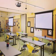 an empty classroom with desks and chairs in front of a projector screen on the wall