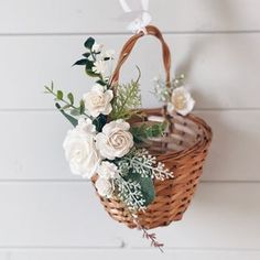 a basket with flowers hanging from the side on a white wooden wall next to a brick wall