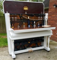 an old piano turned into a wine rack with bottles and glasses on it in front of a brick building