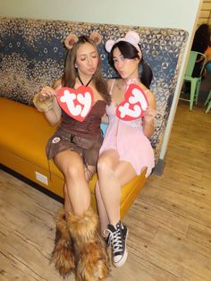 two women dressed in costumes sitting on a couch holding up heart - shaped cutouts