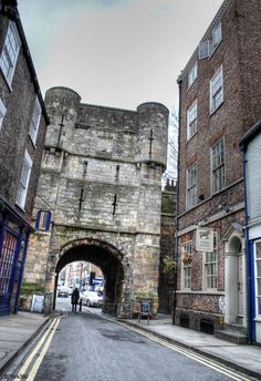 two people are walking down the street in front of an old brick building with a stone arch