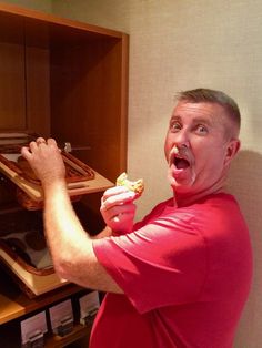 a man in a red shirt is taking a piece of food out of an oven