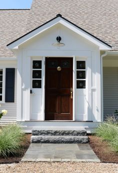 a white house with black shutters and a brown door on the front porch is shown