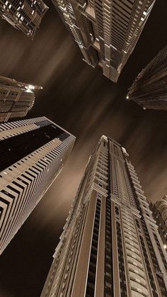 looking up at tall skyscrapers in the city from ground level, with lights shining on them