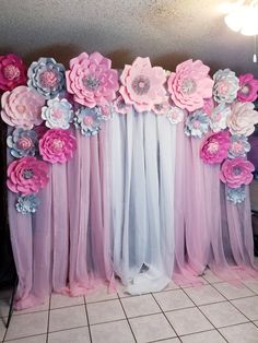 pink and blue flowers are hanging on the wall behind sheer tulle curtains in front of a tiled floor