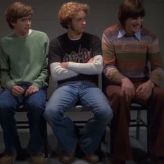 three young men sitting next to each other in front of a wall with their arms crossed