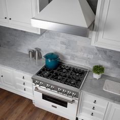 a stove top oven sitting inside of a kitchen next to white cabinets and wooden floors