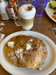 pancakes with butter and syrup on a white plate next to a cup of cappuccino