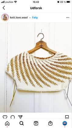 a white and gold knitted shawl hanging on a wooden hanger next to a door