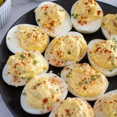 several deviled eggs on a black plate with seasoning sprinkled on top