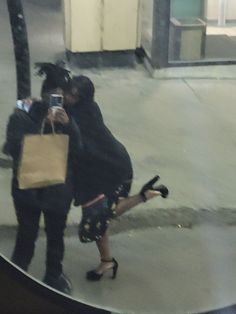 two people are taking pictures on their cell phones as they walk down the street with shopping bags