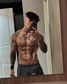 a shirtless man taking a selfie in front of a mirror with tattoos on his chest