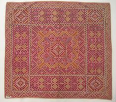 an orange and pink rug with geometric designs on the bottom, in front of a white wall