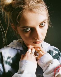 a woman with blue eyes wearing a tie dye sweater and holding her hands to her chest