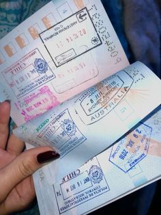 two passport stamps are being held up by someone's hand with red nail polish