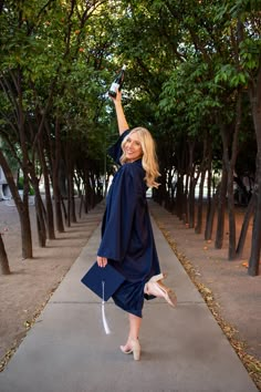 a woman in a graduation gown and cap is holding her arm up to the sky