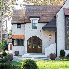 a white brick house with brown trim and two large planters in the front yard