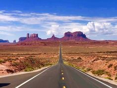 an empty road in the middle of desert with mountains in the backgrouds