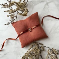 an orange pillow with a ring on it sitting next to some dried flowers and branches