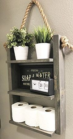 a shelf with some plants and toilet paper on it, hanging from the wall next to two rolls of toilet paper