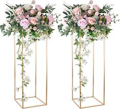 two tall vases with flowers and greenery in them on stands, one is gold