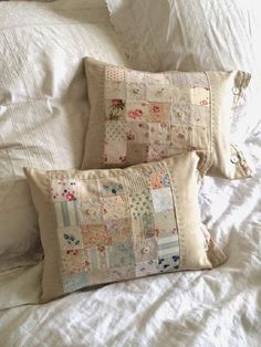 two pillows are on the bed with white linens and quilted material in them