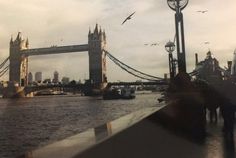 people are walking on the sidewalk next to the water and tower bridge in london, england