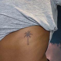 a woman's stomach with a small palm tree tattoo on the side of her belly