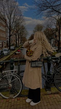 a woman standing next to a bike holding a basket full of fruit in her hands