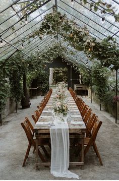 a long table is set up in the middle of an enclosed area with greenery