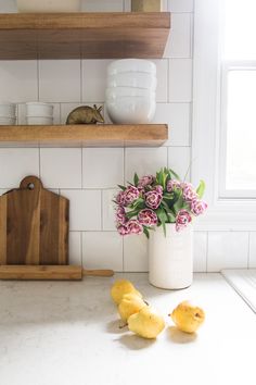 two yellow rubber ducks sitting on a counter next to a vase with flowers in it